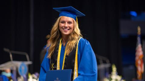 A student walks with her degree at graduation