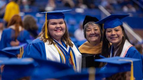 A professor stands with two students at commencement